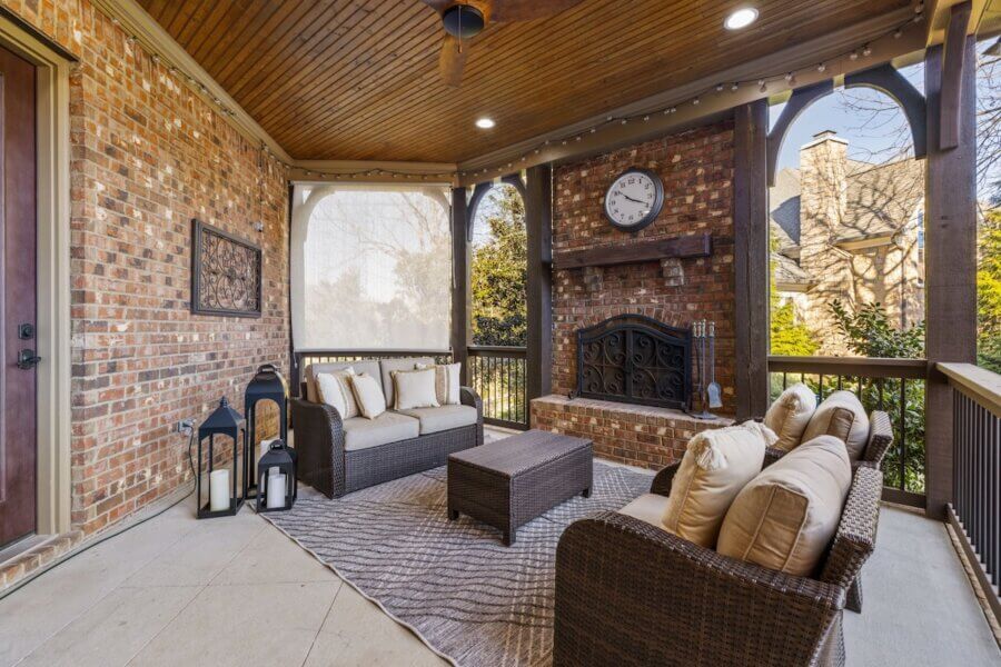 Just Listed! A Franklin Home Designed to Entertain & Unwind - 10 Just listed Franklin home featuring a covered brick patio with wicker furniture, beige cushions, a rug, decorative lanterns, and a fireplace with a clock above it—designed to entertain and surrounded by wooden beams and railings.