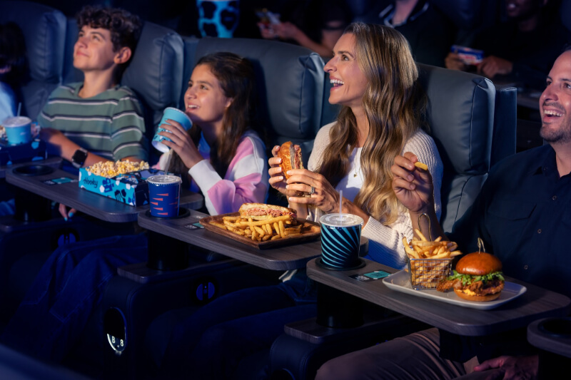 Coming Soon to Nashville! 10 Exciting Additions - 4 In Nashville, four people sit in a movie theater in 2026, enjoying sandwiches, burgers, fries, popcorn, and drinks while watching a movie.