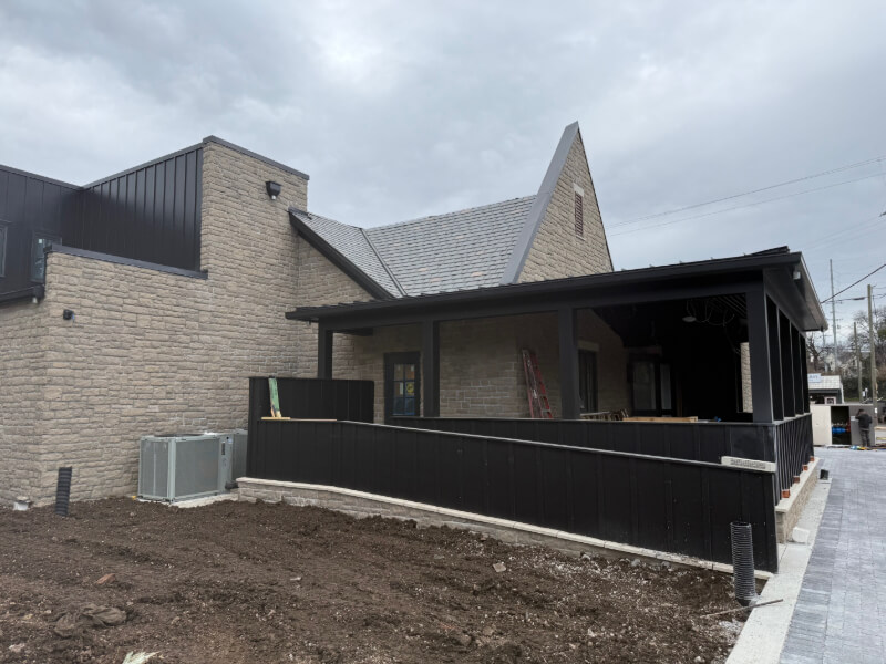 Coming Soon to Nashville! 10 Exciting Additions - 2 A modern stone building with a black metal fence and covered porch stands in Nashville, next to a patch of bare soil beneath a cloudy sky, hinting at changes coming by 2026.