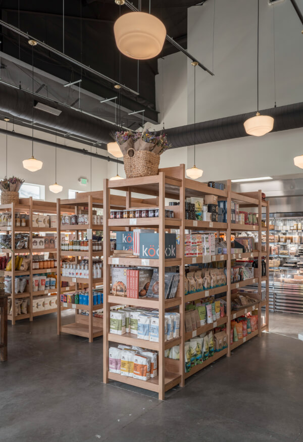 Coming Soon to Nashville! 10 Exciting Additions - 6 Wooden shelves stocked with various packaged goods are arranged in a well-lit Nashville store with high ceilings and hanging lights, offering a modern shopping experience in 2026.