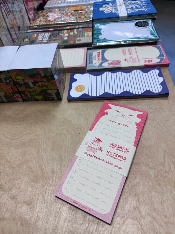 16 Nashville FINDS for a Winter Refresh - 13 Assorted notepads and stationery arranged on a wooden table, featuring a pink cat-shaped notepad labeled "DON'T WANNA" in the foreground—perfect for your latest Nashville FINDS or a Winter Reset of your workspace.