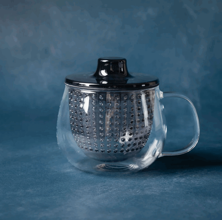 16 Nashville FINDS for a Winter Refresh - 9 A clear glass mug with a handle, containing a metal infuser and covered with a black lid, sits on a blue surface against a matching blue background—perfect for your Winter Reset in Nashville.