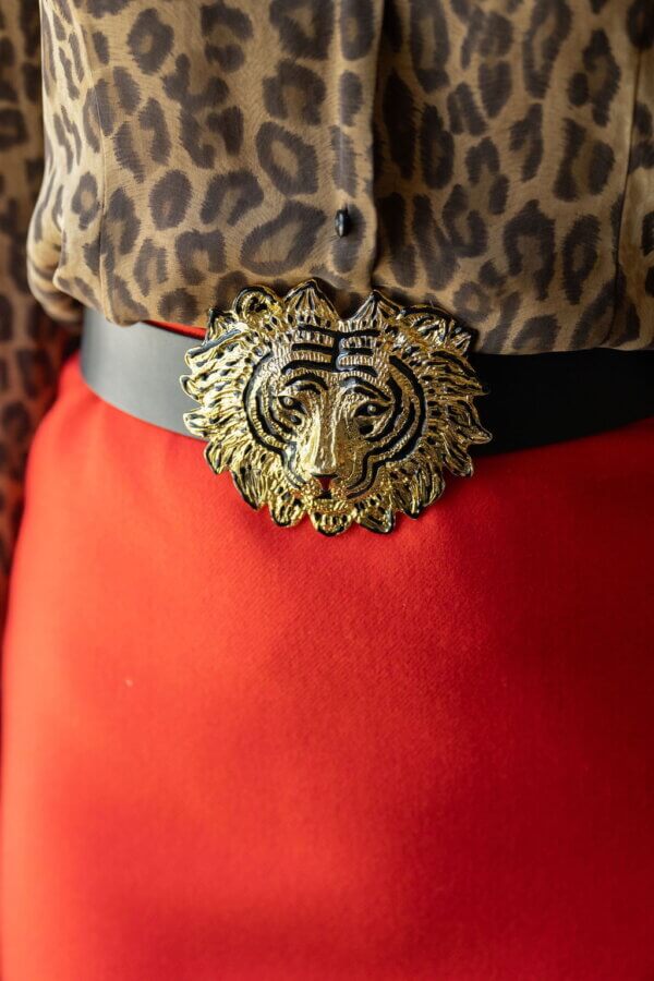 Meet Lindsay Thomas: Founder of Garland Bags - 3 Close-up of a person wearing a leopard print shirt, Garland Bags accessory, a black belt with a gold lion head buckle, and a red skirt.