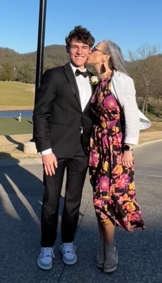 The Goldfinch Foundation Gives Nashville Youth a Lifeline - 6 A young man in a black suit and sneakers stands smiling as a woman in a floral dress and white jacket kisses his cheek outdoors on a sunny day, celebrating with the Goldfinch Foundation.