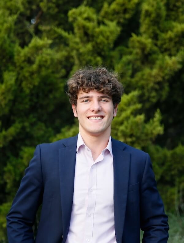 The Goldfinch Foundation Gives Nashville Youth a Lifeline - 3 A young man in a navy blazer and light shirt stands outdoors, smiling, with green trees in the background at a Goldfinch Foundation event hosted by Dr. Elisabeth Willers.