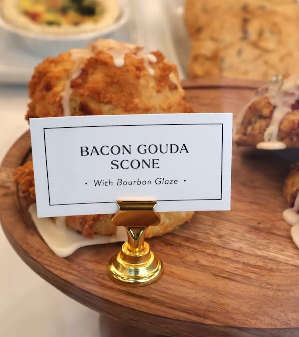 A wooden tray holds a bacon gouda scone drizzled with glaze. A small sign in front reads "Bacon Gouda Scone with Bourbon Glaze"—a tempting treat inspired by new Nashville restaurants.