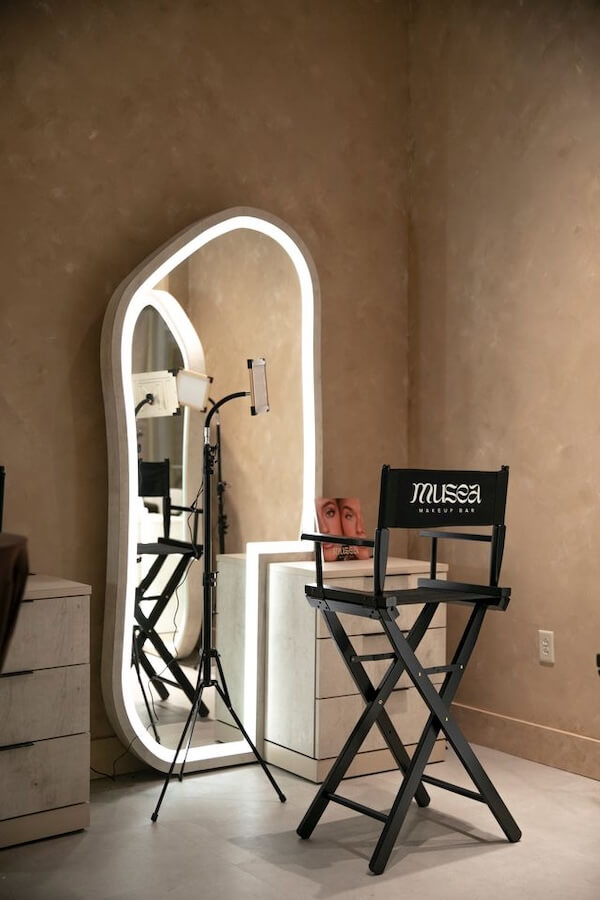 6 New Nashville Services to Elevate Your Everyday - 5 A beauty studio corner with a large illuminated mirror, a black "Musea Beauty Bar" chair, a ring light on a stand, and a small cabinet with a face art piece—perfect for experiencing new Nashville services.