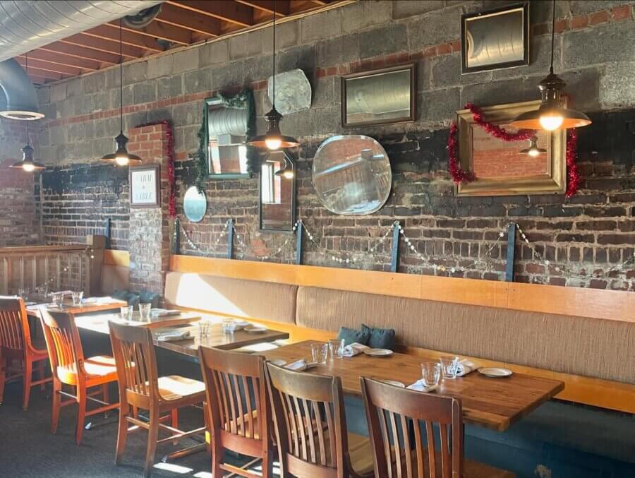An Ode to Margot Cafe: Au Revoir Mon Amie - 3 A sunlit Margot Cafe interior features wooden tables and chairs, exposed brick walls, hanging lights, and assorted mirrors and frames on the wall.