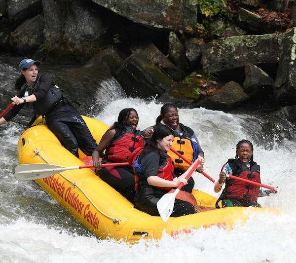 8 Adventurous Girls' Trips (All Skill Levels!) - 6 Five people in life jackets paddle a yellow raft through whitewater rapids, surrounded by rocks and splashing water—perfect for adventurous girls trips seeking excitement and unforgettable memories.
