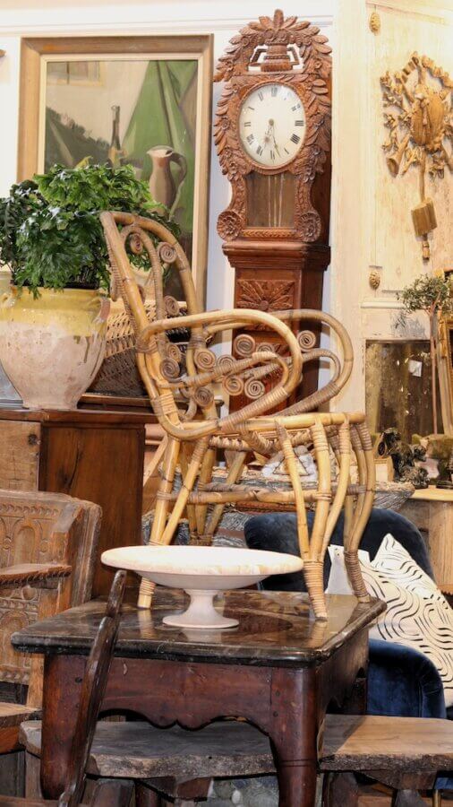 Meet Staci Davidman of Atlanta's Beloved Foxgloves Antiques - 4 Assorted vintage furniture and decor items from foxglove antiques, including wicker chairs, a grandfather clock, framed artwork, and a potted plant, displayed in an antique shop.