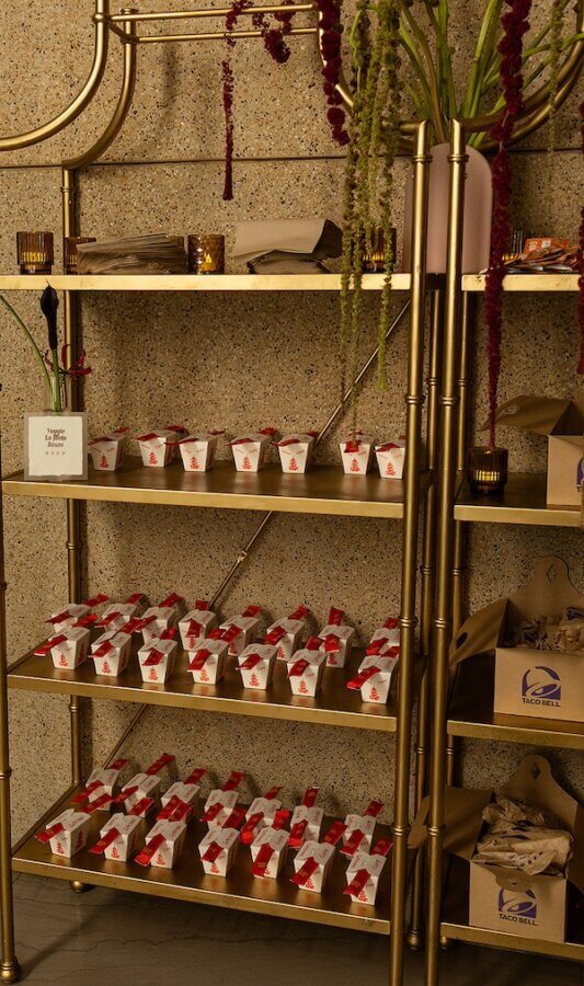 A Gold-Washed Wedding at Nashville's Iconic Parthenon - 17 Gold shelves at this Golden Parthenon wedding display rows of white takeout and Taco Bell boxes, accented by candles and floral arrangements atop the speckled wall backdrop.