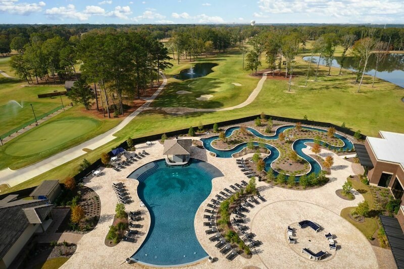 Mississippi, Reimagined: A Different Kind of Spring Break Guide - 5 Aerial view of a Mississippi resort pool area with lounge chairs, a curving lazy river, and golf course—perfect for Spring Break fun amidst trees and scenic ponds in the background.