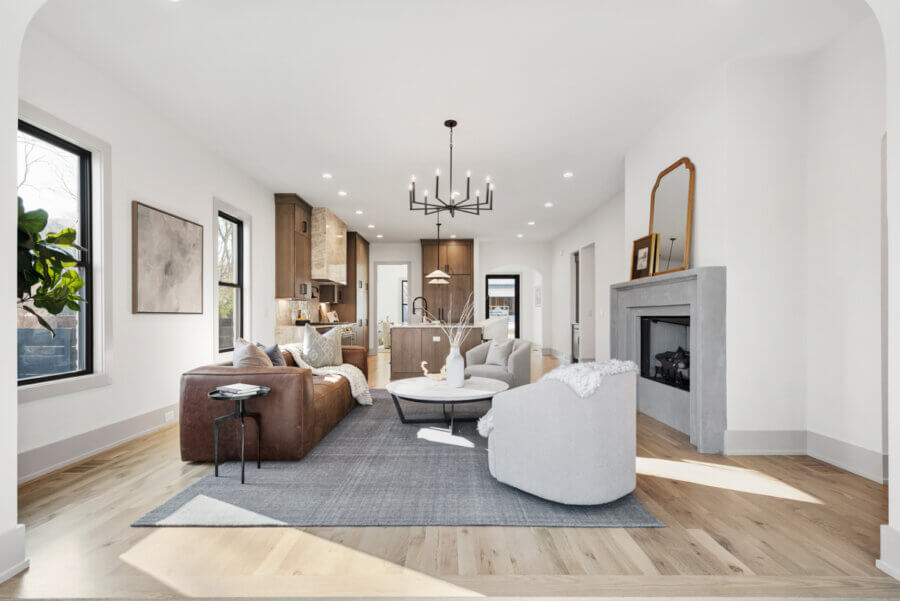 Modern open-concept living room and kitchen at 506 Stonewall Way, Brentwood TN, featuring neutral tones, contemporary furniture, a fireplace, large windows, and a chandelier above a round coffee table.