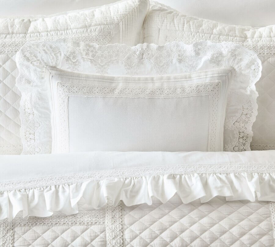Trend Alert: Lace is Back! - 27 White bed with quilted and lace-trimmed pillows and a comforter, featuring detailed embroidery and ruffled edges.