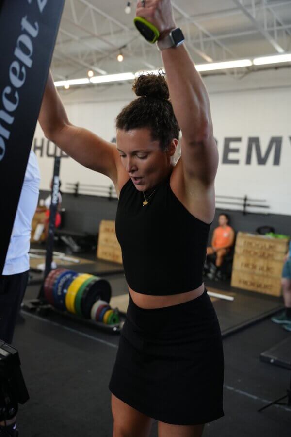 Meet the Co-Founder of Birmingham's "Recovery House" - 2 Kelly Nguyen in athletic wear exercises indoors at RCVRY House, gripping overhead handles in a gym with weights and boxes in the background.