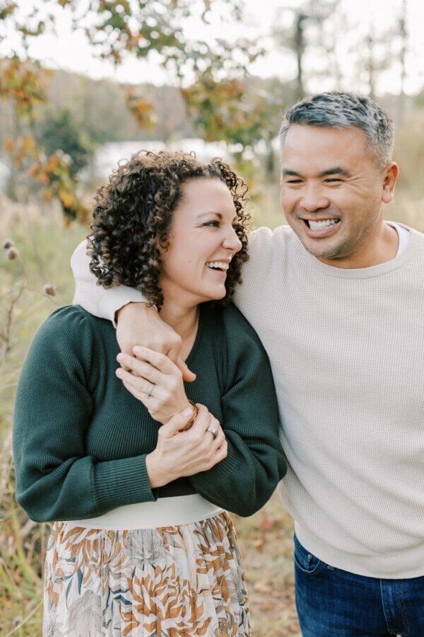 Meet the Co-Founder of Birmingham's "Recovery House" - 3 A smiling man with his arm around a smiling woman, both standing outdoors in front of trees and foliage, share a joyful moment at RCVRY House.