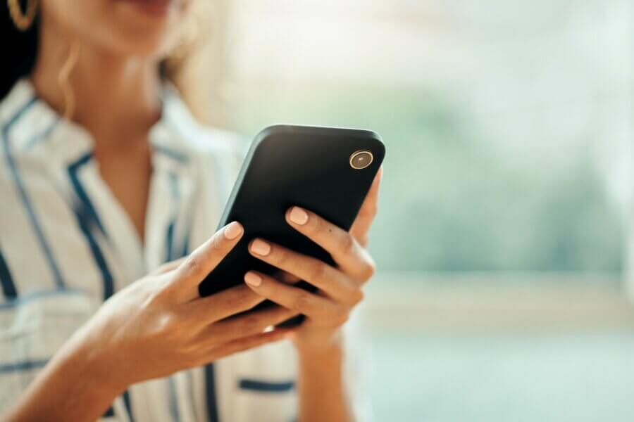 The Money Moves That Matter Most for Women (in Every Decade!) - 2 A person holding and using a smartphone, wearing a striped shirt, with a blurred backgroundβperfectly capturing the modern woman seeking financial advice for women on-the-go.