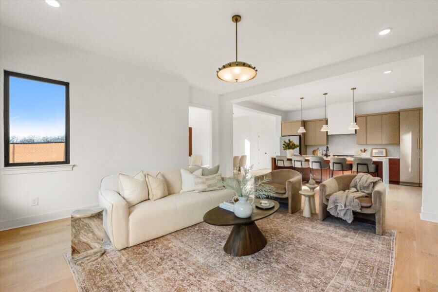 Modern open-concept living room and kitchen in Richmond Bnd, featuring a beige sofa, armchairs, coffee table, pendant lights, and a large window with natural light—perfect for Nashville real estate seekers.