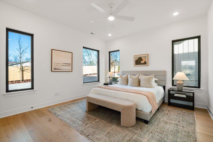 Modern Nashville bedroom with large windows, a neatly made bed, two nightstands with lamps, neutral decor, and hardwood floors at 627 Richmond Bnd.