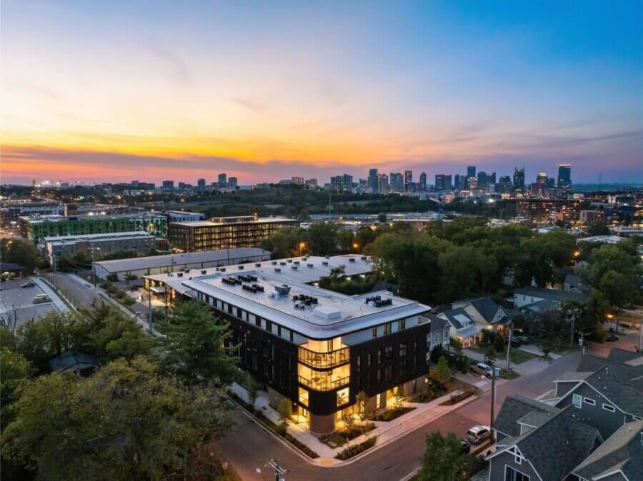 A modern apartment building at 506 Merritt Ave is shown at dusk, with the Nashville city skyline and residential homes in the background under a colorful sky.