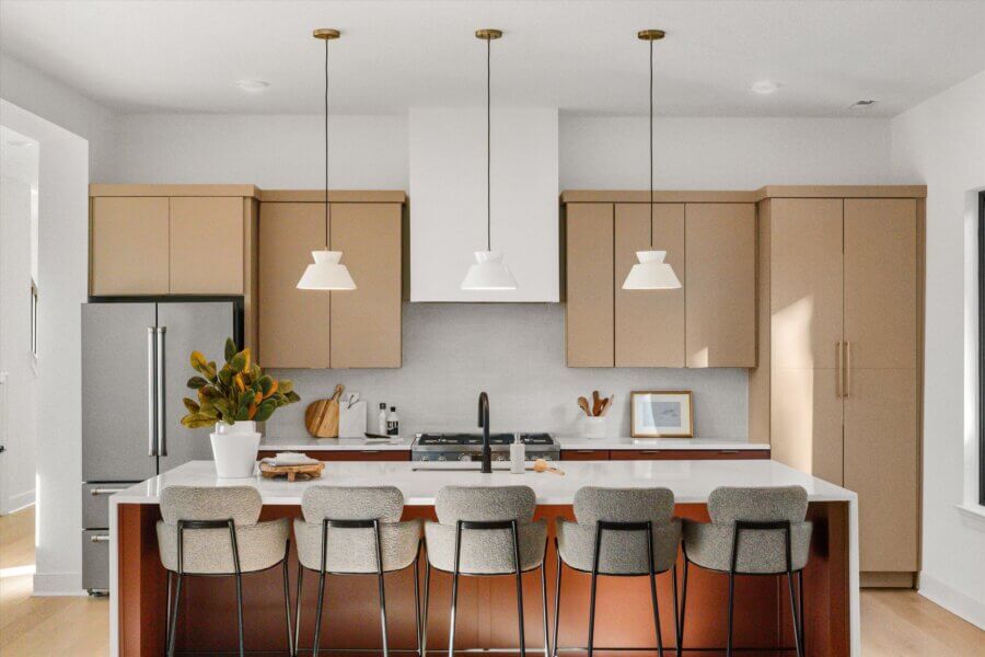Modern kitchen at 627 Richmond Bnd in Nashville TN, featuring beige cabinets, stainless steel appliances, a white island with five gray barstools, pendant lights, and a potted plant on the counter.