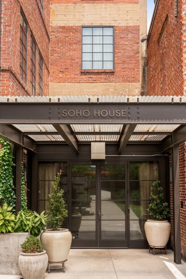 Entrance to Soho House at 506 Merritt Ave, Nashville TN, featuring brick walls, glass double doors, potted plants, and a "SOHO HOUSE" sign above the entrance.