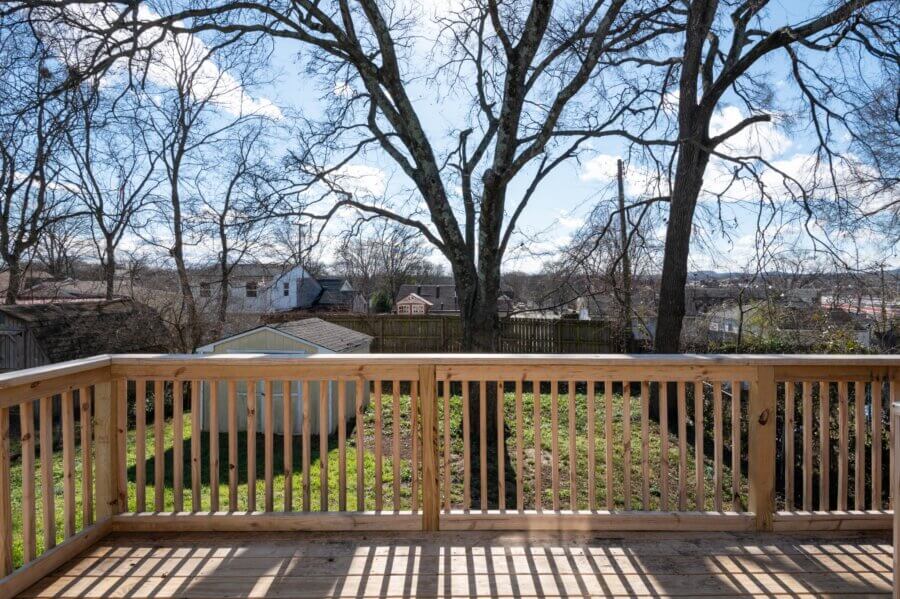 Wooden deck with railing overlooks a backyard with trees, a shed, and a small vegetable garden at 112 Wiley St in Madison TN, with neighboring houses and a clear blue sky in the background.