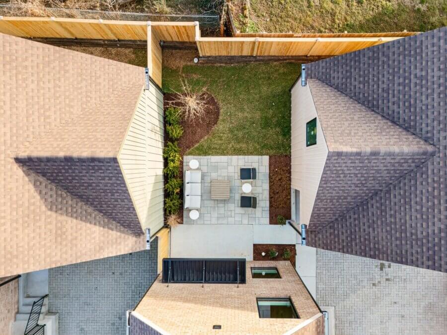 Aerial view of a fenced backyard with a paved patio, outdoor furniture, and surrounding grass between two houses at 627 Richmond Bnd, Nashville TN.