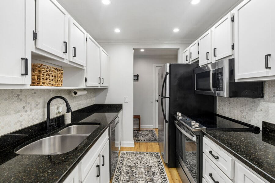 Modern galley kitchen in Nashville featuring white cabinets, black appliances, granite countertops, and a patterned rug on a wooden floor—perfect for contemporary living at 4425 Westlawn Dr.