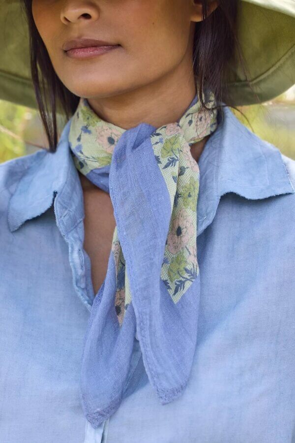 6 Spring 2026 Fashion Trends + How to Wear Them - 5 A person wearing a light blue button-up shirt, a wide-brimmed hat, and a light blue scarf with a floral pattern tied around their neck.