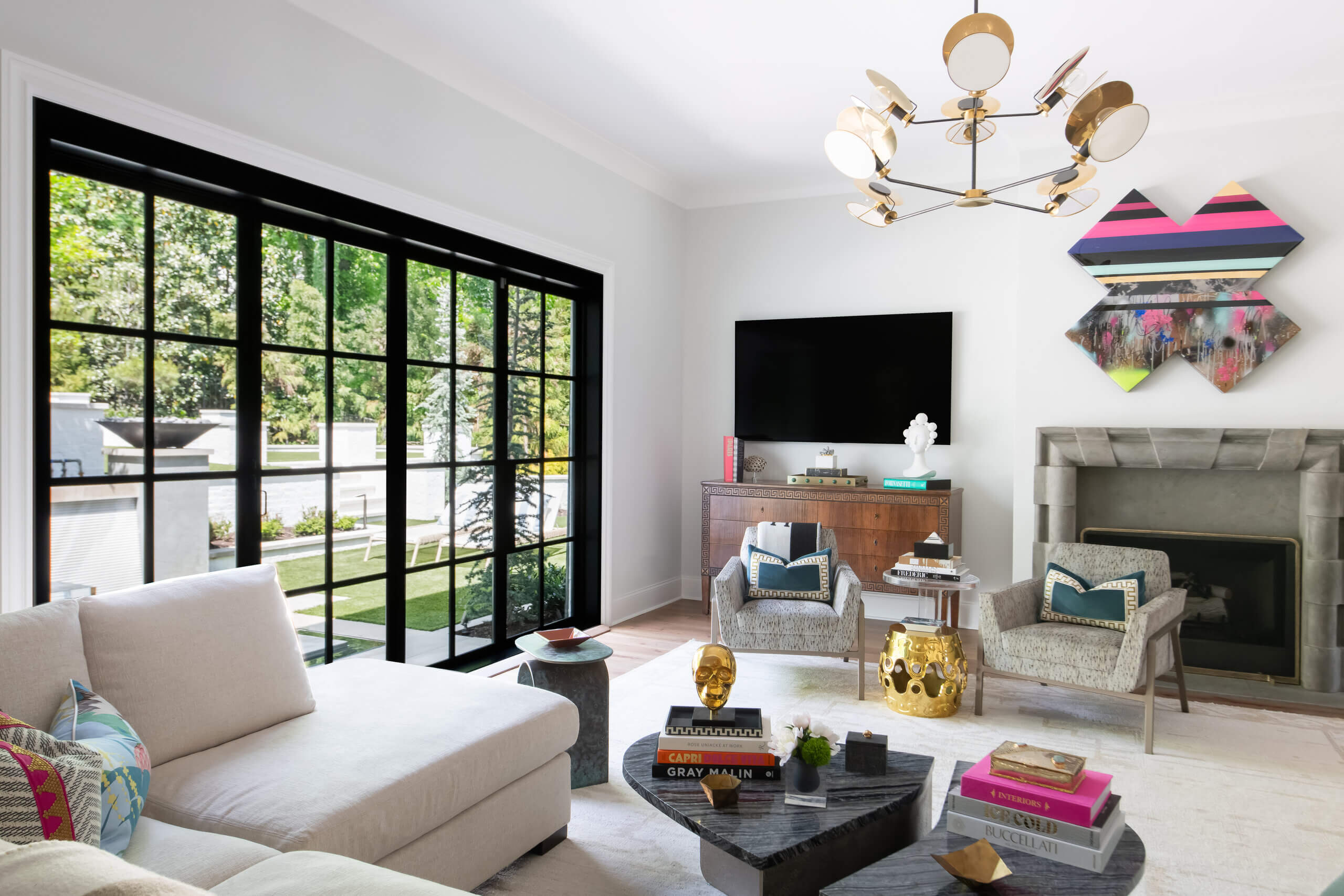 Modern living room by JASPER Builds featuring large black-framed windows, white walls, contemporary furniture, geometric decor, and a wall-mounted TV above a wooden console.