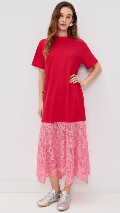 6 Spring 2026 Fashion Trends + How to Wear Them - 9 A person stands against a white wall wearing a red T-shirt dress with a pink lace hem and silver sneakers, effortlessly showcasing how to wear spring trends and embrace Spring 2026 fashion trends.