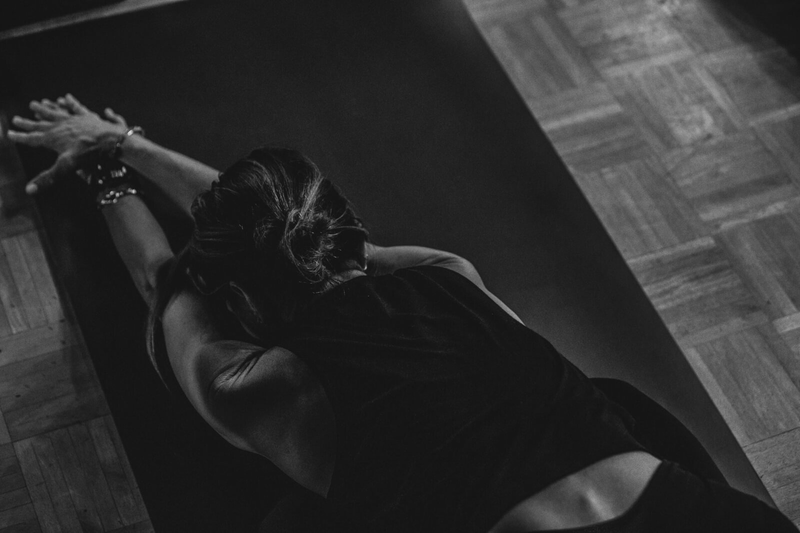 Person performing a forward stretch on a yoga mat, arms extended forward, head down, photographed from above in black and white—an image capturing the essence of the PM Method for mindful movement. ARCHIVE.