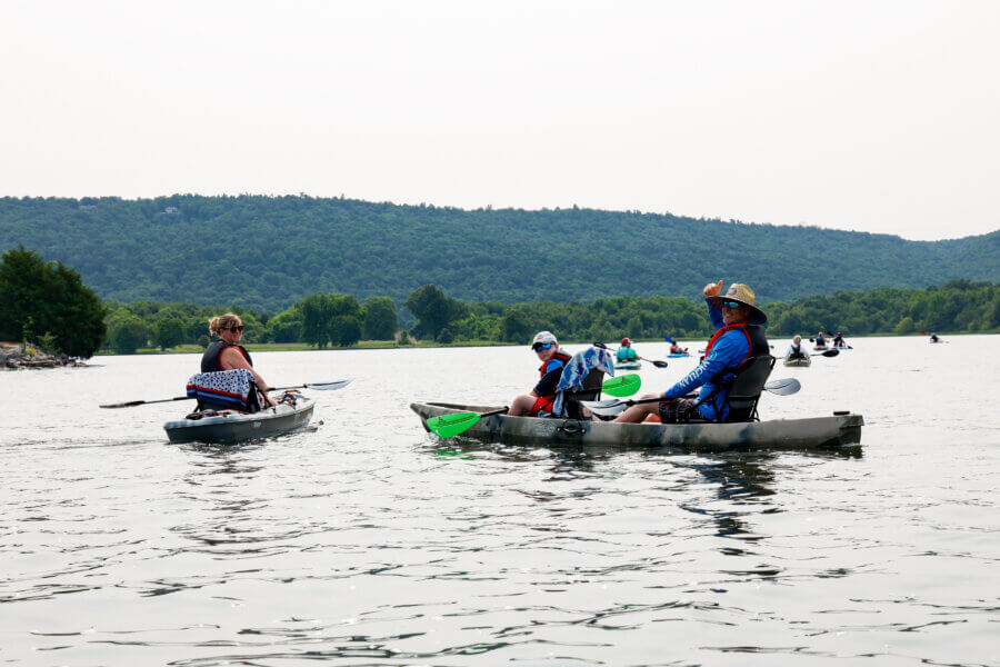 52 Weekends, 630 Miles: Alabama’s Scenic River Trail is the Longest in the Country - 2 Several people kayak on a calm lake along the Alabama Scenic River Trail, with forested hills in the background under a bright sky—perfect for weekends on the water.