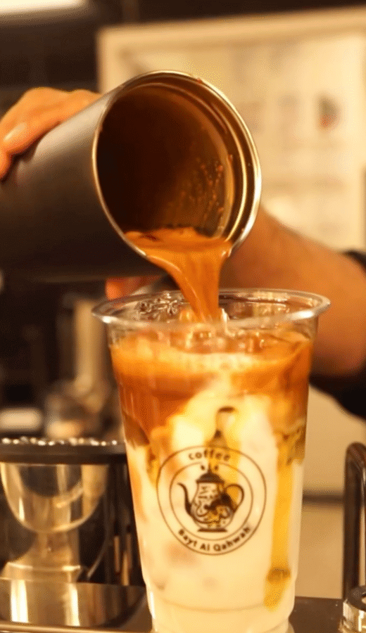 10 New Birmingham Restaurants to Try This Month - 14 A barista pours espresso from a metal shaker into a clear cup filled with milk and ice, creating a layered coffee drink.