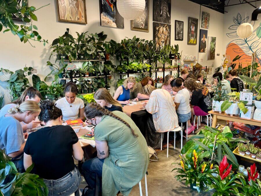 Meet Jessica Watts of BHAM's House Plant Collective - 6 A group of people sits at tables in a plant-filled room, engaging in arts and crafts activities surrounded by house plants and artwork on the walls, echoing the creative spirit of Jessica Watts and House Plant Collective.