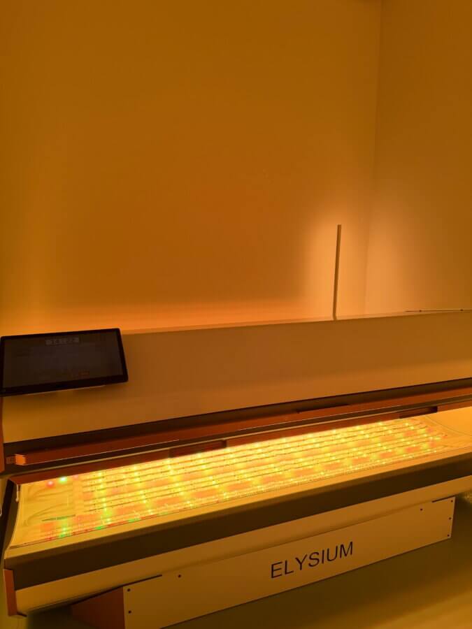 Her BHAM Clinic Blends Holistic Healing with Medical Expertise - 5 A light therapy bed labeled "ELYSIUM" emits yellow and red light in a dimly lit room at Sparrow Clinic.