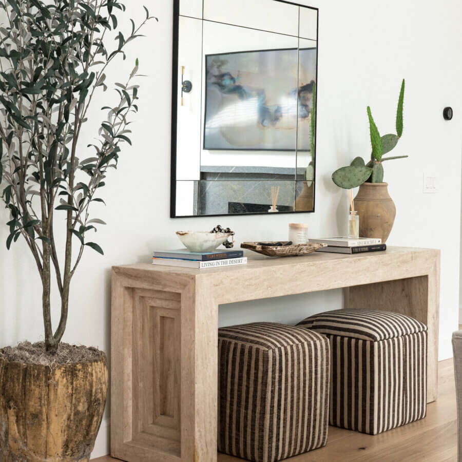 Step Inside an Austin Interior Designer’s Home - 4 A wooden console table with two striped ottomans underneath, decor items on top, a large potted plant to the left, and a wall mirror above creates a personal retreat inspired by an Austin interior designer’s touch.