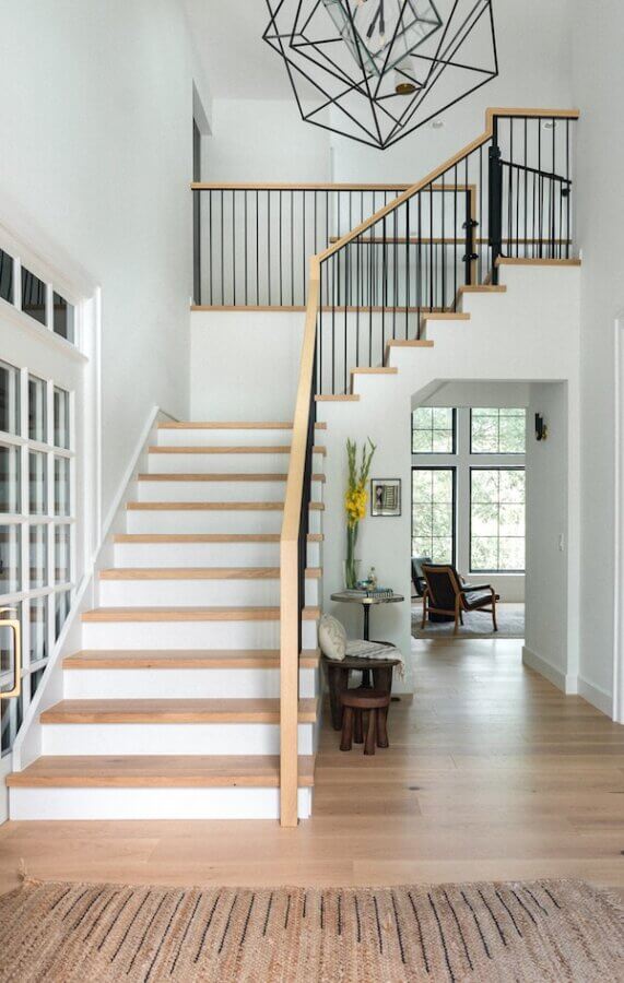 Step Inside an Austin Interior Designer’s Home - 5 Modern entryway designed by an Austin interior designer, featuring a wooden staircase, metal railing, geometric light fixture, light wood floors, and a cozy sitting area by tall windows.