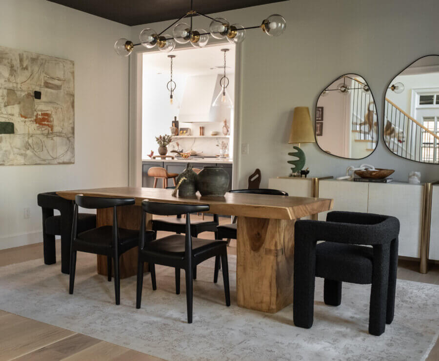 Step Inside an Austin Interior Designer’s Home - 14 A modern dining room designed by an Austin interior designer features a wooden table, six black chairs, abstract wall art, two irregular mirrors, and a view into a bright kitchen.