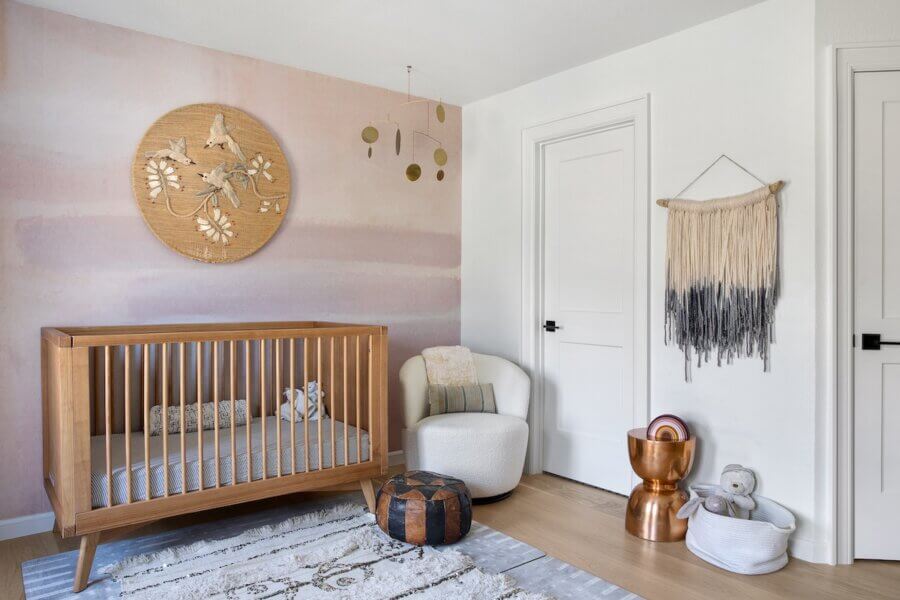 Step Inside an Austin Interior Designer’s Home - 11 A modern nursery designed by an Austin interior designer, featuring a wooden crib, white armchair, pouf, and toys. Pastel walls, decorative wall art, and a hanging mobile create a serene personal retreat for your little one.