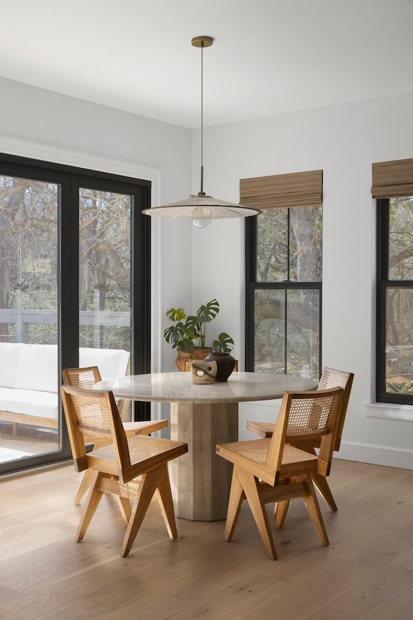 Step Inside an Austin Interior Designer’s Home - 7 A round wooden dining table with three chairs sits by large windows, styled by an Austin interior designer as a personal retreat, with a plant and decor atop the table and outdoor seating visible through the glass door.