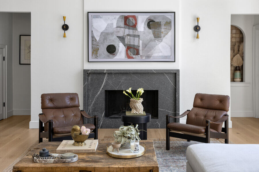 Step Inside an Austin Interior Designer’s Home - 3 Modern living room designed by an Austin interior designer, featuring two brown leather chairs, a black marble fireplace, abstract art, and decorative items on a wooden coffee table—perfect for a personal retreat.