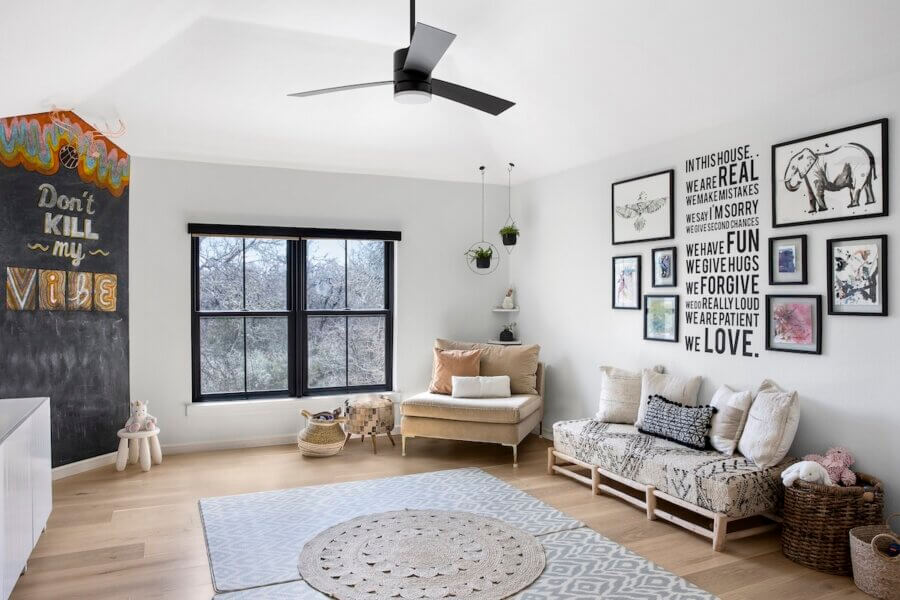 Step Inside an Austin Interior Designer’s Home - 12 Bright, modern room with large windows, a sofa, armchair, wall art, and a chalkboard with colorful writing; designed by an Austin interior designer as a personal retreat with neutral decor, light wood floors, and a ceiling fan.