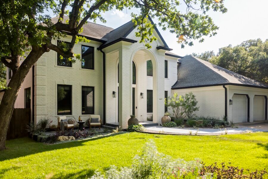 Step Inside an Austin Interior Designer’s Home - 16 Two-story white brick house with large front columns, arched entryway, black trim windows, double garage, and a landscaped front yard.