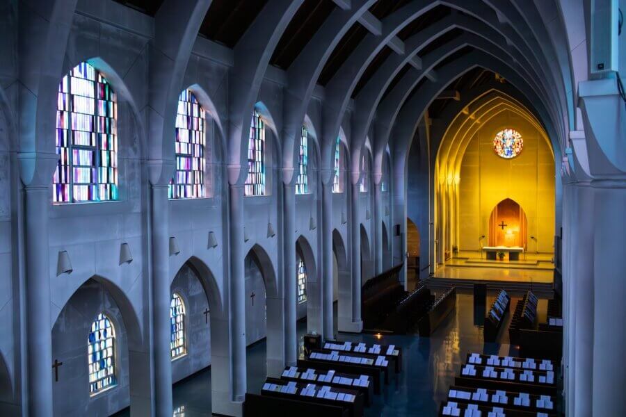 How to Eat, Shop & Explore Your Way Through Georgia - 11 Interior of a church in Georgia with arched ceilings, stained glass windows, rows of pews, and an illuminated altar at the front beneath a circular stained glass window. A peaceful place to visit while you Eat Shop Play Georgia.