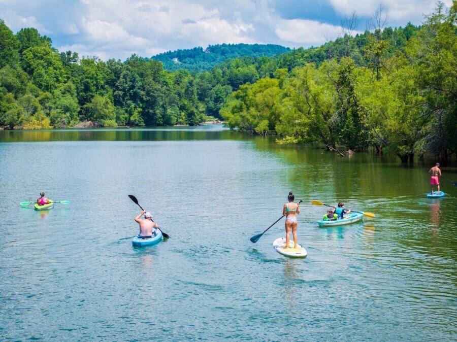 9 Hidden Gems to Visit in the South - 7 Five people paddle on stand-up paddleboards and kayaks on a calm lake surrounded by green trees under a partly cloudy sky—a hidden gem in the South.