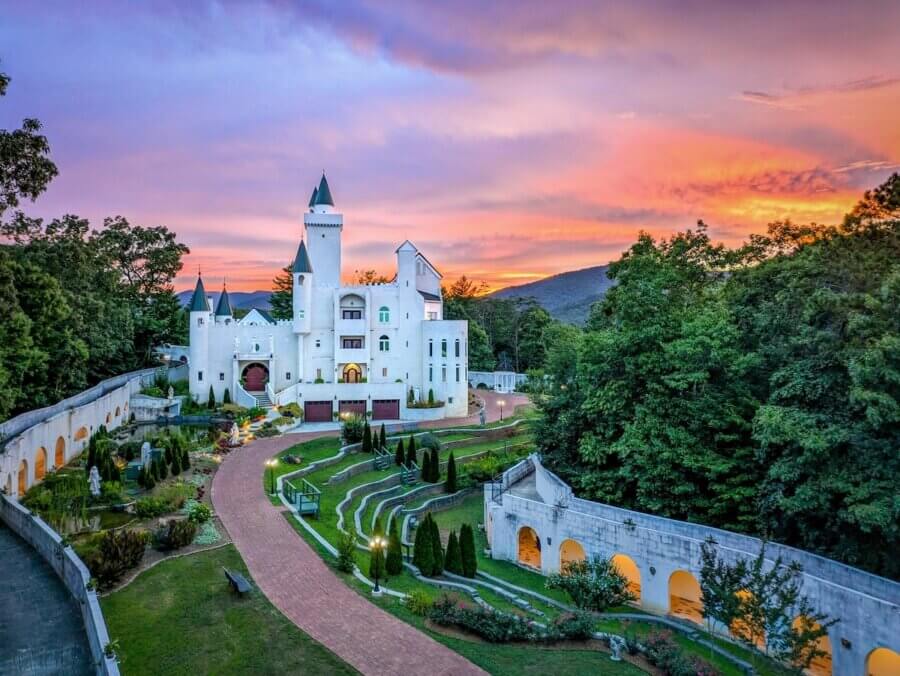 9 Hidden Gems to Visit in the South - 9 A white castle-style building with green rooftops stands among trees at sunset in the South, with terraced gardens, curved walkways, and a colorful sky—a true hidden gem waiting to be discovered.