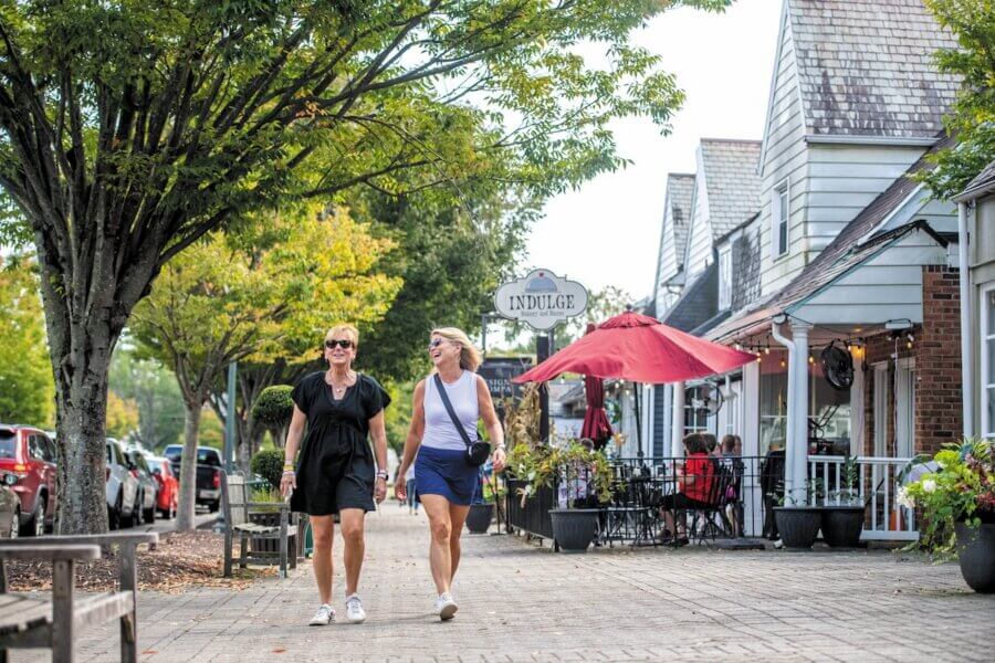 9 Hidden Gems to Visit in the South - 11 Two women walk and talk on a tree-lined sidewalk in a small town shopping area.