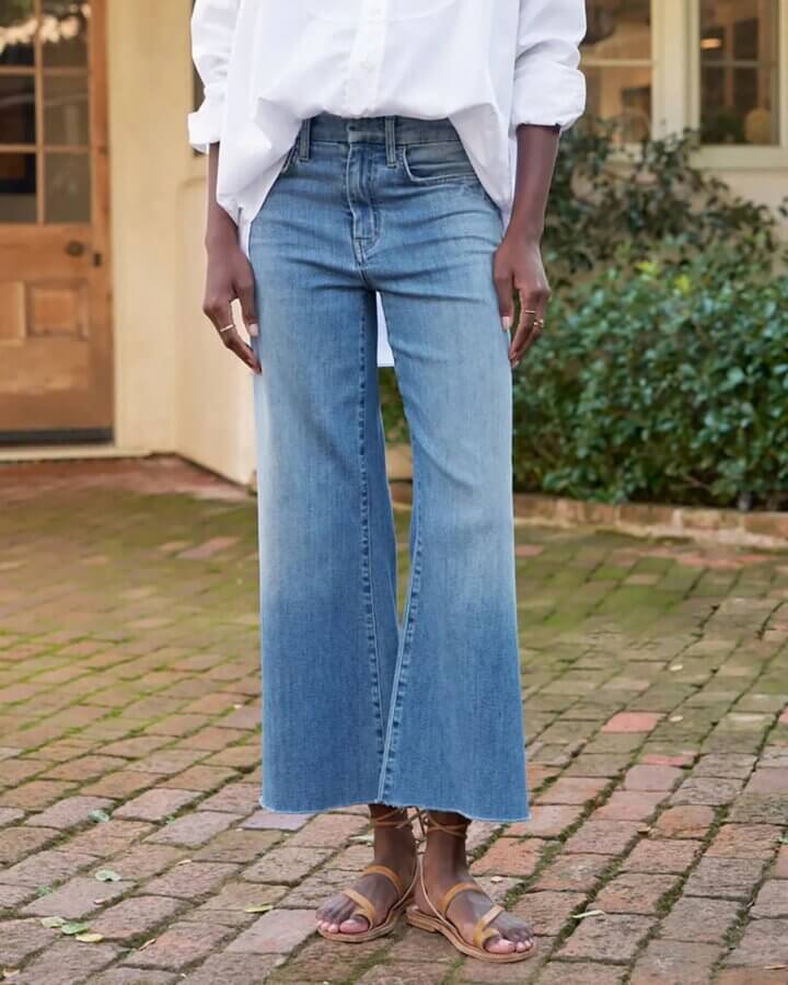 15 Memphis FINDS to Welcome Spring - 4 Person wearing a white shirt, light blue wide-leg jeans, and brown sandals stands on a brick path in front of a house with greenery—one of our favorite Memphis finds this February.